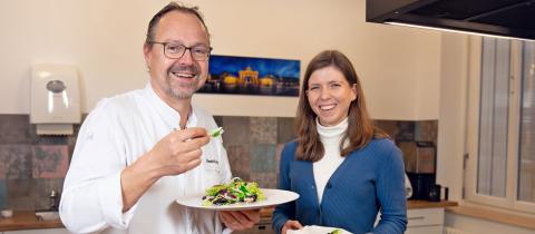 Verena Kaiser and Hendrik Otto in their kitchen, holding up plates with healthy food
